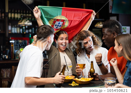 Happy international sport fans waving the flag of Portugal while drinking beer and watching tournament in sport bar Happy international sport fans waving the flag of Portugal while drinking beer and watching tournament in sport bar 105450621