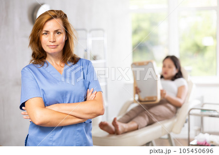 Woman beautician wearing blue overall posing in clinic of esthetic medicine Woman beautician wearing blue overall posing in clinic of esthetic medicine 105450696