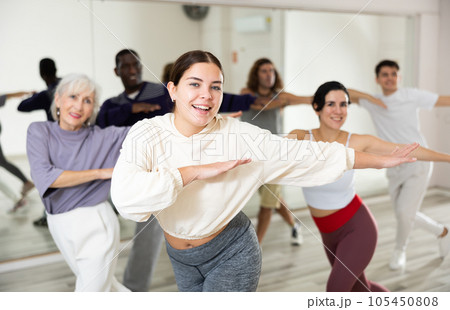 Happy young woman practising modern dance moves with other people in dance studio 105450808