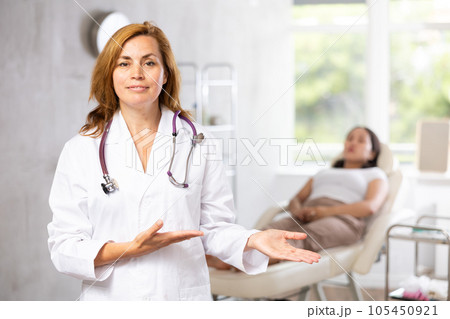 Portrait of female doctor cosmetologist wearing white overall showing equipment of clinic before procedure Portrait of female doctor cosmetologist wearing white overall showing equipment of clinic before procedure 105450921