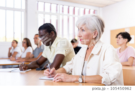 Positive elderly woman listening and taking notes during language courses Positive elderly woman listening and taking notes during language courses 105450962
