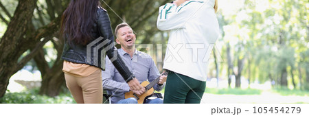 Happy deceased man in wheelchair playing ukulele for his friends in the park. 105454279