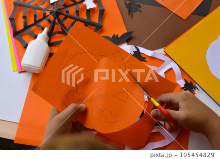 Close-up of children's hands that create paper crafts for Halloween. Homemade decorations for the holiday. Close-up of children's hands that create paper crafts for Halloween. Homemade decorations for the holiday. 105454829