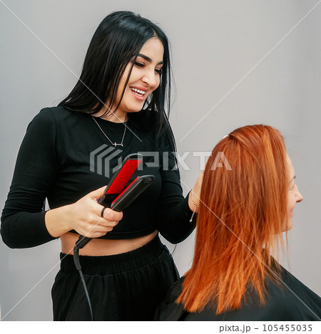 Woman hairdresser makes basal volume to client of beauty salon. Professional stylist straightens Woman hairdresser makes basal volume to client of beauty salon. Professional stylist straightens 105455035