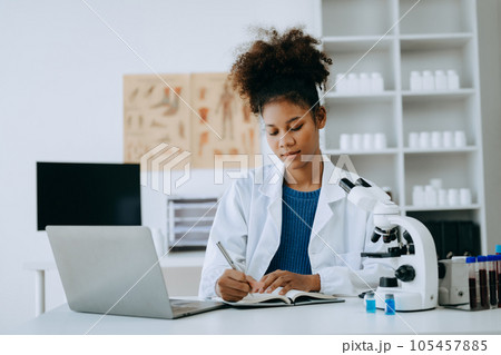 African smiling doctor or consultant sitting at a desk his neck writing sick note, surgery planning and prescription.and clinical report test results in office..looking at the camera African smiling doctor or consultant sitting at a desk his neck writing sick note, surgery planning and prescription.and clinical report test results in office..looking at the camera 105457885