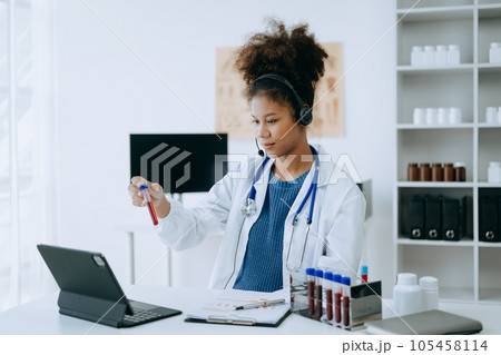 Attractive African female doctor talking while explaining medical treatment to patient through a video call with laptop in office or laboratory 105458114