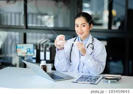 Concentrated dentist sitting at table with jaw samples tooth model and working with tablet and laptop in dental office professional dental clinic. 105459643