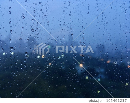 Raindrops on glass with cityscape in the background blurred and the background city bokeh light. City life in the rainy season evening, abstract urban background.  105461257