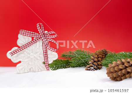 White shiny snowflake with bow, fir branches and cones on snow, red background behind. Christmas, New Year, winter. Copy space 105461597