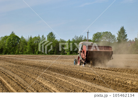 Potato planter is hitched to tractor during planting of potatoes during spring sowing period in plowed farmer field. 105462134