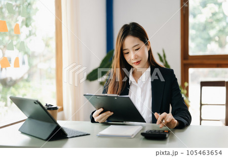 Beautiful Asian business woman typing laptop and tablet Placed at the table at the office.. Beautiful Asian business woman typing laptop and tablet Placed at the table at the office.. 105463654