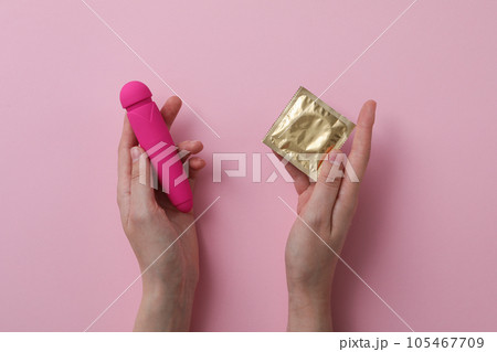 Condom and pink vibrator in hand on pink background 105467709