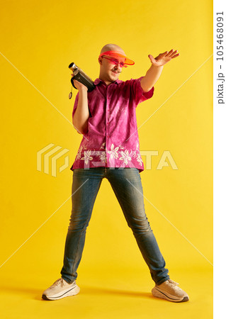 Image of full lengh young man in bright cap and t-shirt reguleting process of shooting on vintage camera against bright yellow background. Image of full lengh young man in bright cap and t-shirt reguleting process of shooting on vintage camera against bright yellow background. 105468091