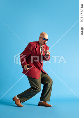 Full lenght image. Balded man with mustache dressed in business retro suit sneaking over blue studio background. 105468188