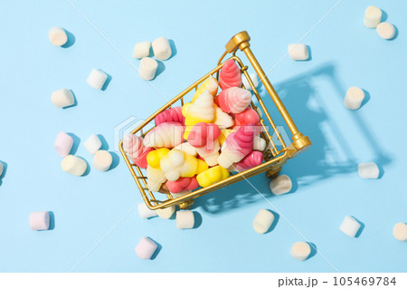 Jelly candies in shopping trolley and marshmallows on blue background, top view Jelly candies in shopping trolley and marshmallows on blue background, top view 105469784