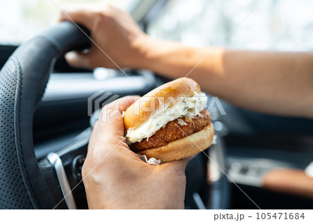 Asian lady holding hamburger to eat in car, dangerous and risk an accident. 105471684