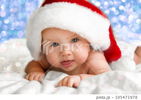 Beautiful little child is celebrating Christmas. New Year's holidays. A child in a Christmas costume. Childhood and people concept - happy Newborn baby in Santa hat over holidays lights background 105471978