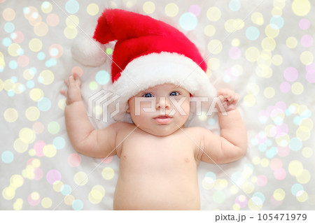 Beautiful little child is celebrating Christmas. New Year's holidays. A child in a Christmas costume. Childhood and people concept - happy Newborn baby in Santa hat over holidays lights background 105471979