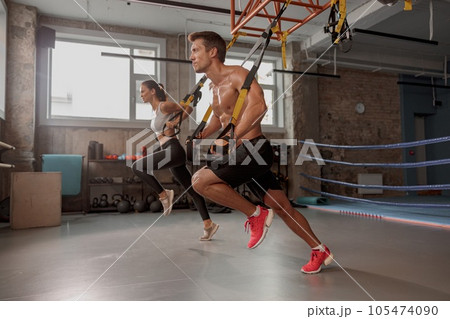 Muscular man in the gym with athletic woman performing sports exercises 105474090