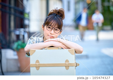 キャリーバックの前で座っている旅先の若い女性 キャリーバックの前で座っている旅先の若い女性 105474327