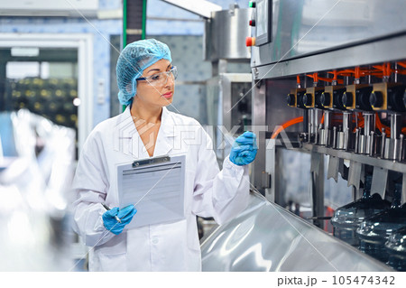 Bottling factory worker inspecting quality of water bottles before shipment. Reverse osmosis system used in plant. water purity and maintaining quality control in bottling process. High quality photo 105474342