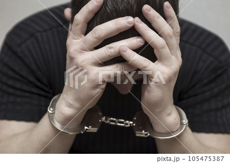 Handcuffed man covering his face with his hands. 105475387