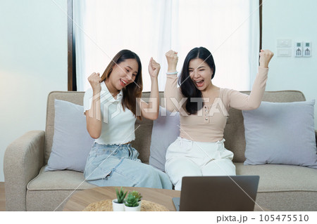 lgbtq, lgbt concept, homosexuality, portrait of two asian women posing happy together and loving each other while playing computer laptop on sofa. lgbtq, lgbt concept, homosexuality, portrait of two asian women posing happy together and loving each other while playing computer laptop on sofa. 105475510