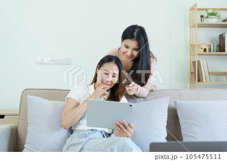 lgbtq, lgbt concept, homosexuality, portrait of two asian women posing happy together and loving each other while playing tablet at sofa. lgbtq, lgbt concept, homosexuality, portrait of two asian women posing happy together and loving each other while playing tablet at sofa. 105475511