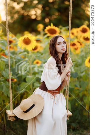 Woman in a dress in a field of sunflowers on a swing 105475878