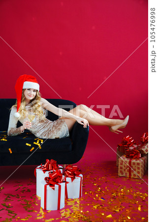 woman in santa hat with champagne and sparklers in red room on sofa with canfeti woman in santa hat with champagne and sparklers in red room on sofa with canfeti 105476998
