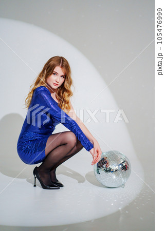 woman in shiny blue dress on floor with a disco ball on a white room 105476999
