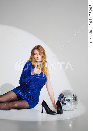woman in shiny blue dress on floor with champagne and disco ball on a white room woman in shiny blue dress on floor with champagne and disco ball on a white room 105477007