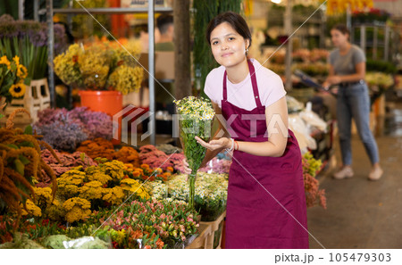 Portrait of a positive female flower market seller with bouquet of daisies for buyers Portrait of a positive female flower market seller with bouquet of daisies for buyers 105479303