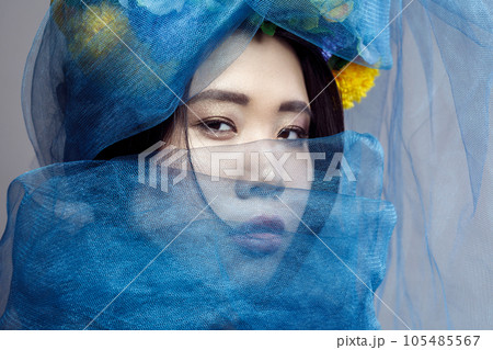 Closeup portrait of concentrated attentive attractive sensual beautiful woman with floral hat, female with makeup, hiding her face with blue veil. Indoor studio shot isolated on gray background, 105485567