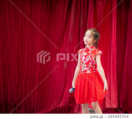 The Asian kid girl sing a song on stage at her school activity day, dress in Qipao style, red curtain background 105485724