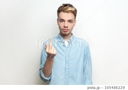Portrait of rude serious impolite man wearing denim shirt showing middle finger, arguing with somebody, looking at camera with bossy expression. Indoor studio shot isolated on gray background. 105486229