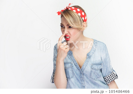 You are liar. Portrait of funny foolish blonde woman wearing blue denim shirt and red headband standing touching her nose, frowning face. Indoor studio shot isolated on gray background. You are liar. Portrait of funny foolish blonde woman wearing blue denim shirt and red headband standing touching her nose, frowning face. Indoor studio shot isolated on gray background. 105486466