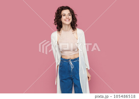 Portrait of extremely happy delighted smiling woman with curly hair wearing casual style outfit standing looking away with positive expression. Indoor studio shot isolated on pink background. Portrait of extremely happy delighted smiling woman with curly hair wearing casual style outfit standing looking away with positive expression. Indoor studio shot isolated on pink background. 105486518