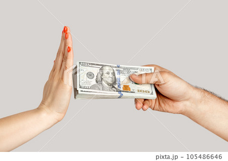 Closeup of woman hand refusing money, man hand offering dollar banknotes, corruption. showing Indoor studio shot isolated on gray background. 105486646