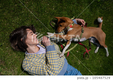 Top view of beautiful young woman and african basenji dog lying on green grass.  105487529