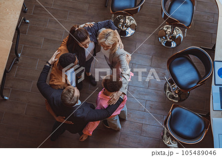 Top view of team of successful colleagues laughing and hugging while standing in circle in coworking Top view of team of successful colleagues laughing and hugging while standing in circle in coworking 105489046