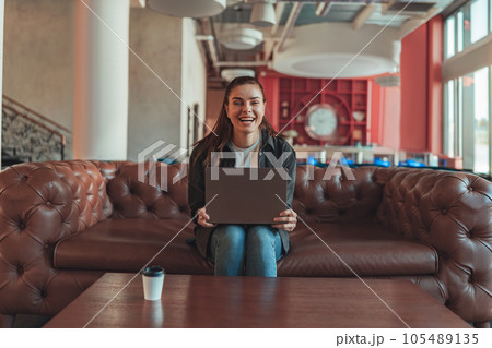 Smiling woman sales manager sitting on sofa and working on laptop on coworking background 105489135