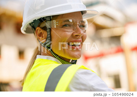Smiling female construction worker in protective helmet standing against on construction background Smiling female construction worker in protective helmet standing against on construction background 105490024
