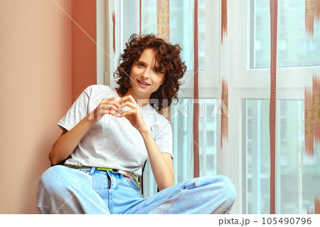 Cheerful woman sitting by window and smiling 105490796