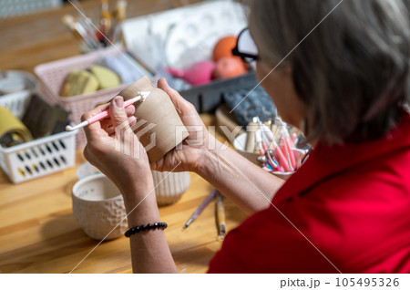 Unrecognizable woman painting on earthenware in pottery workshop, decorating clay products. Unrecognizable woman painting on earthenware in pottery workshop, decorating clay products. 105495326