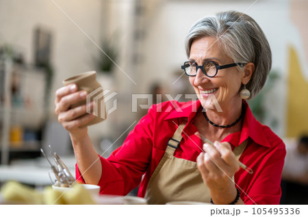 Woman enjoying creative process of pottery coloring in pottery workshop. 105495336