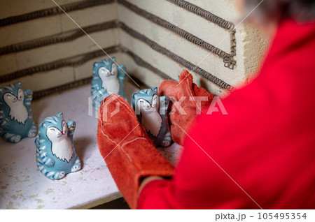 Mature craftswoman taking clay products from pottery kiln 105495354
