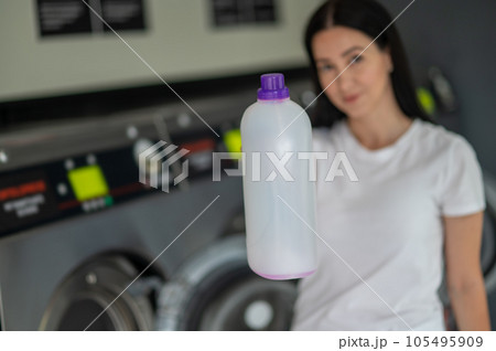 Young woman holding detergent using washing machine. Young woman holding detergent using washing machine. 105495909