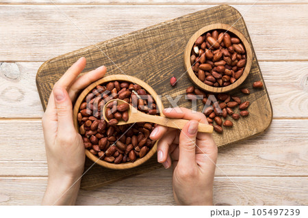 Woman hands holding a wooden bowl with peanuts. Healthy food and snack. Vegetarian snacks of different nuts 105497239