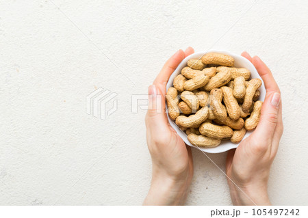 Woman hands holding a wooden bowl with close peanuts. Healthy food and snack. Vegetarian snacks of different nuts 105497242